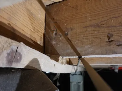 Close-up of wooden beams and joists in a crawl space or basement with visible nails and support.